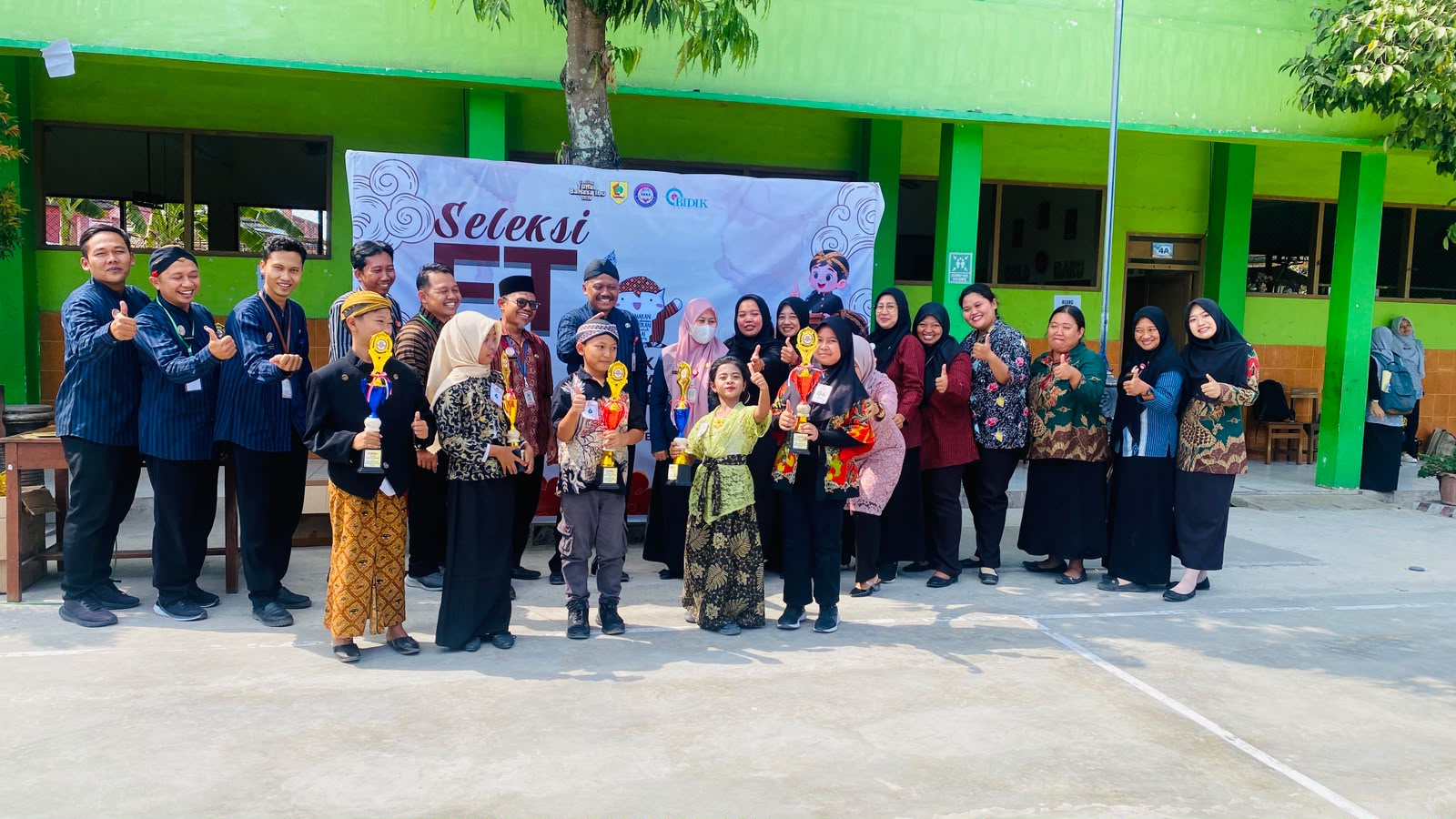 Siswa SD Negeri 2 Baturetno menunjukkan trofi kemenangan didampingi para guru dalam ajang Festival Tunas Bahasa Ibu (FTBI) Tingkat Kecamatan Baturetno di halaman sekolah, Kamis (17/9/2026). Sekolah ini berhasil membawa pulang sejumlah gelar juara dari berbagai cabang lomba.